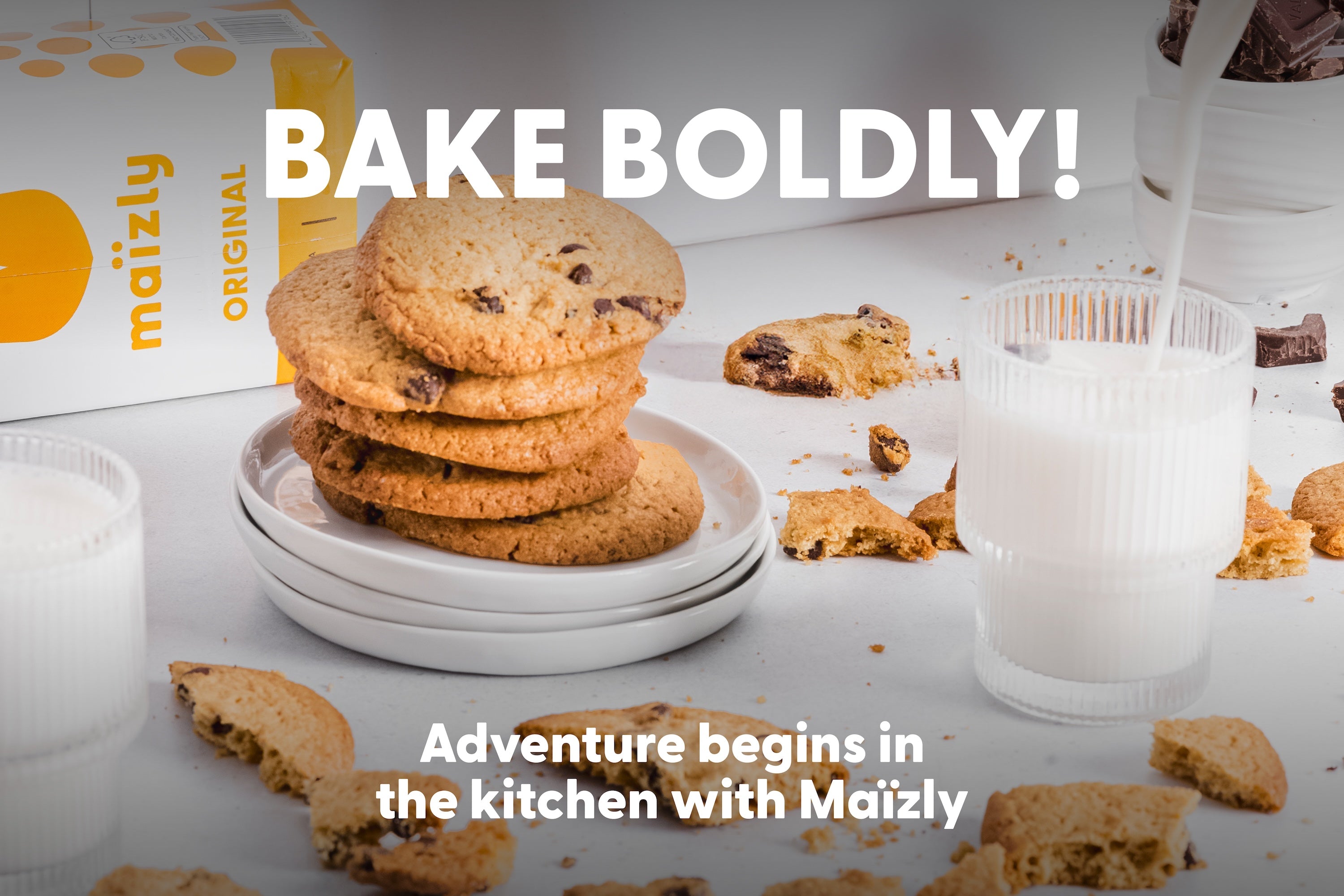 A stack of freshly baked chocolate chip cookies on a plate next to a glass of Maïzly Original corn milk being poured, with crumbs and chocolate scattered around, and the text 'Bake Boldly! Adventure begins in the kitchen with Maïzly.